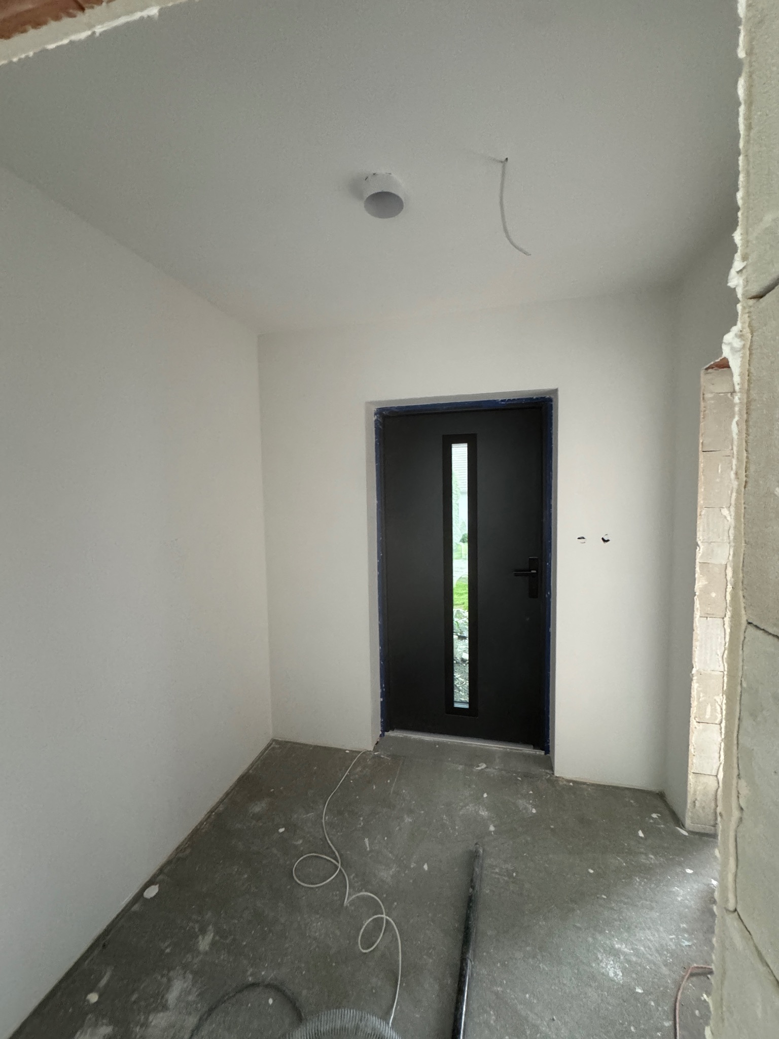 Radziechowy: Wnętrze w trakcie prac wykończeniowych. Ściany pomalowane na biało, widoczna czarna stolarka drzwiowa i fragment ściany z surowej cegły.