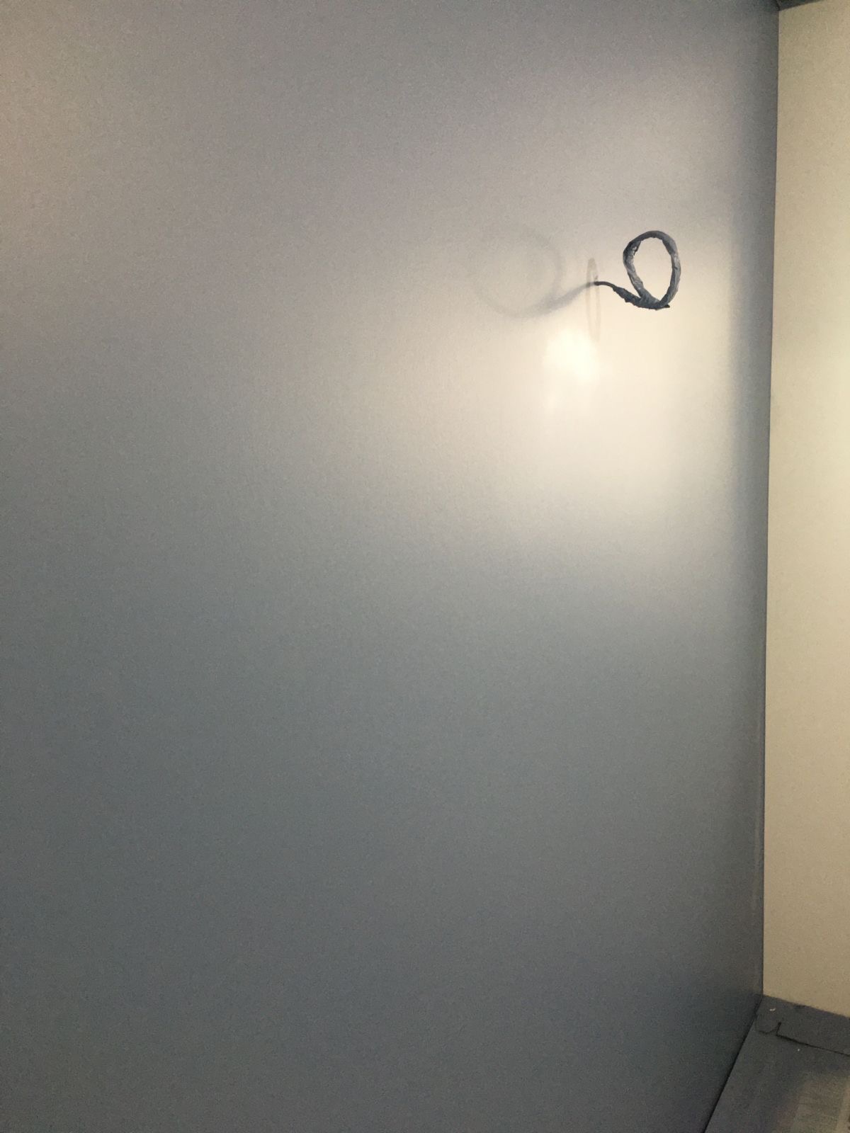 Świeżo pomalowana szara ściana z wystającym kablem elektrycznym zwiniętym w pętlę, widoczny narożnik pokoju i fragment listwy przypodłogowej.