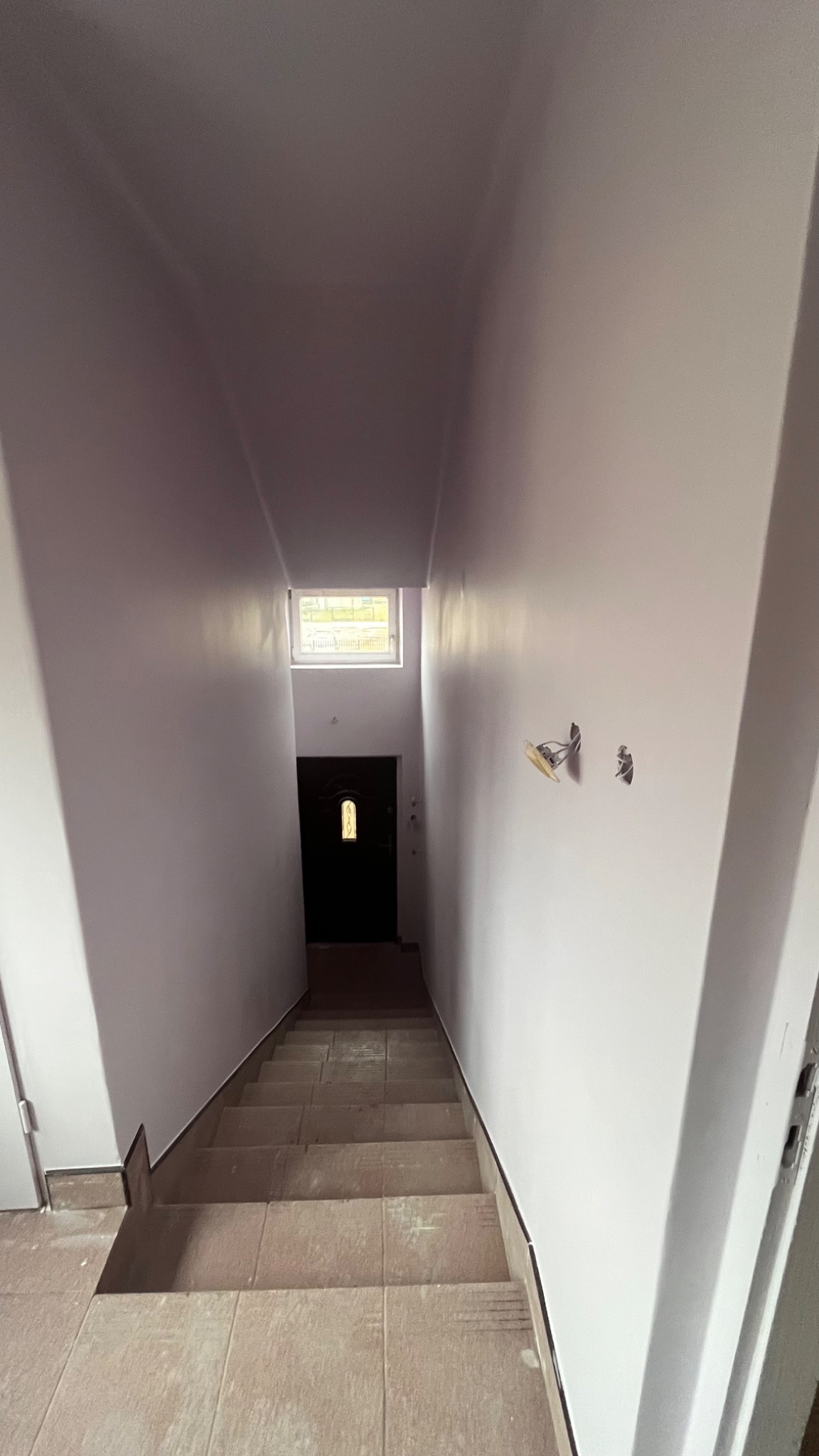 Klatka schodowa po malowaniu na jasny kolor, widoczne niedokończone prace przy podłodze i wystające przewody elektryczne.