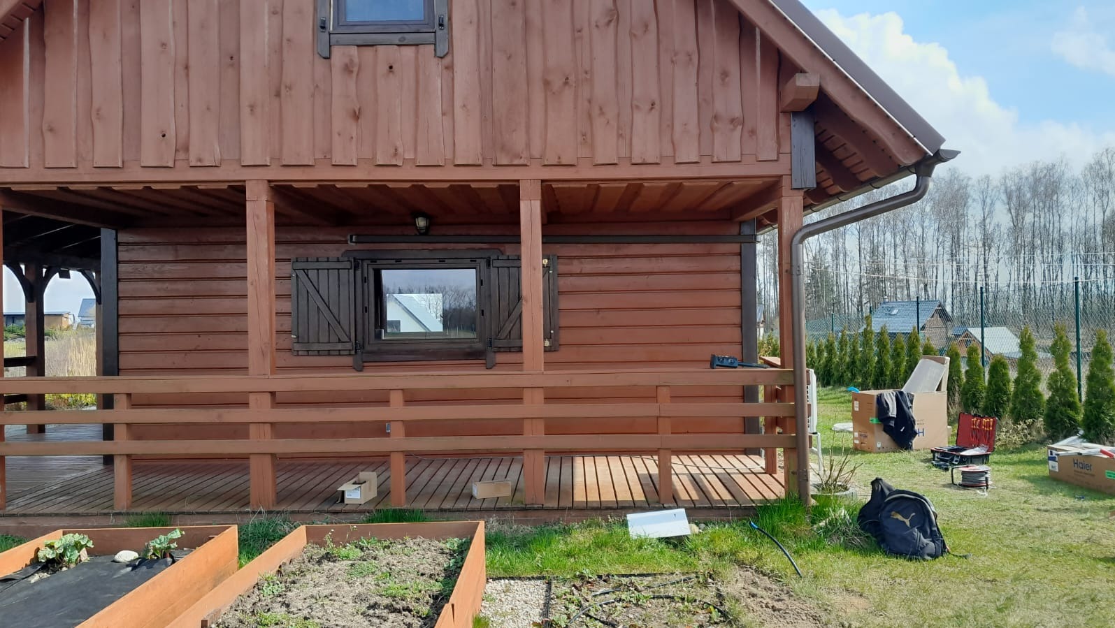 Brązowy, drewniany dom z werandą, widoczne narzędzia i kartony, prawdopodobnie podczas instalacji klimatyzacji.