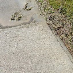 Michał Chojnacki - Mokry chodnik z resztkami trawy i ziemi po czyszczeniu, przylegający do trawnika. Widoczne ślady po strumieniu wody i pozostałości po usuniętych zabrudzeniach.