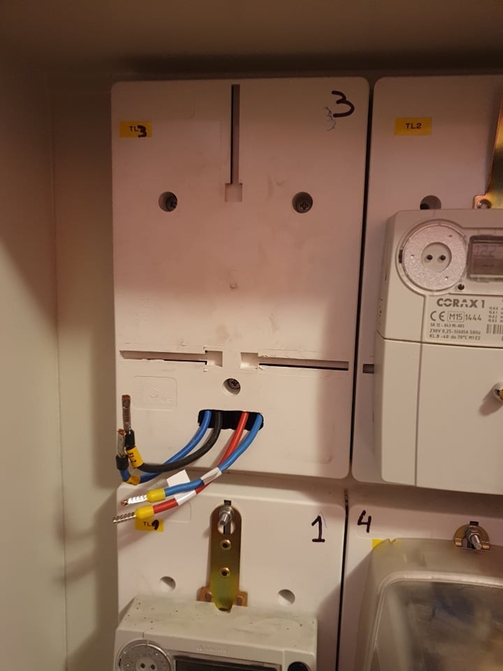 Podłączenie przewodów elektrycznych (niebieski, czarny, czerwony) z oznaczeniami TL do białej skrzynki z numerami 3 i 1/4 wewnątrz rozdzielnicy elektrycznej, widoczny licznik energii.