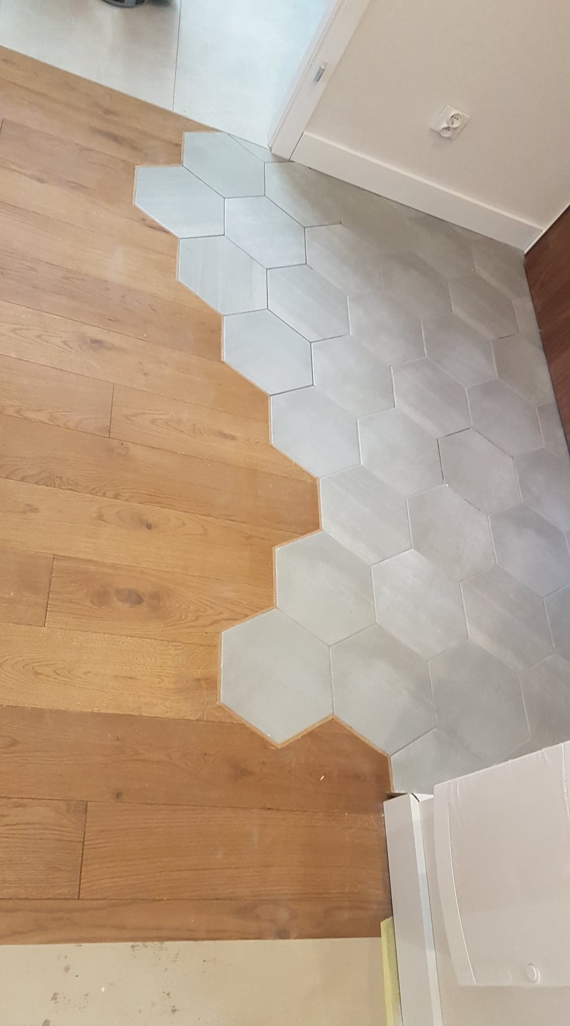 Połączenie drewnianej podłogi z szarymi, heksagonalnymi płytkami podłogowymi, widoczne przejście między materiałami.