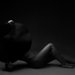 FotoŚliwka.pl - Czarno-białe zdjęcie kobiety leżącej na podłodze, zakrywającej twarz dużym, czarnym kapeluszem o szerokim rondzie; dłonie widoczne trzymają kapelusz, na palcu pierścionek.