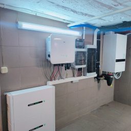 NOVEL ENERGY SP. Z O.O. - Kompletna instalacja fotowoltaiczna w pomieszczeniu: inwerter, rozdzielnica, akumulatory GOODWE, rury i przewody. Widok na ścianę z płytkami.