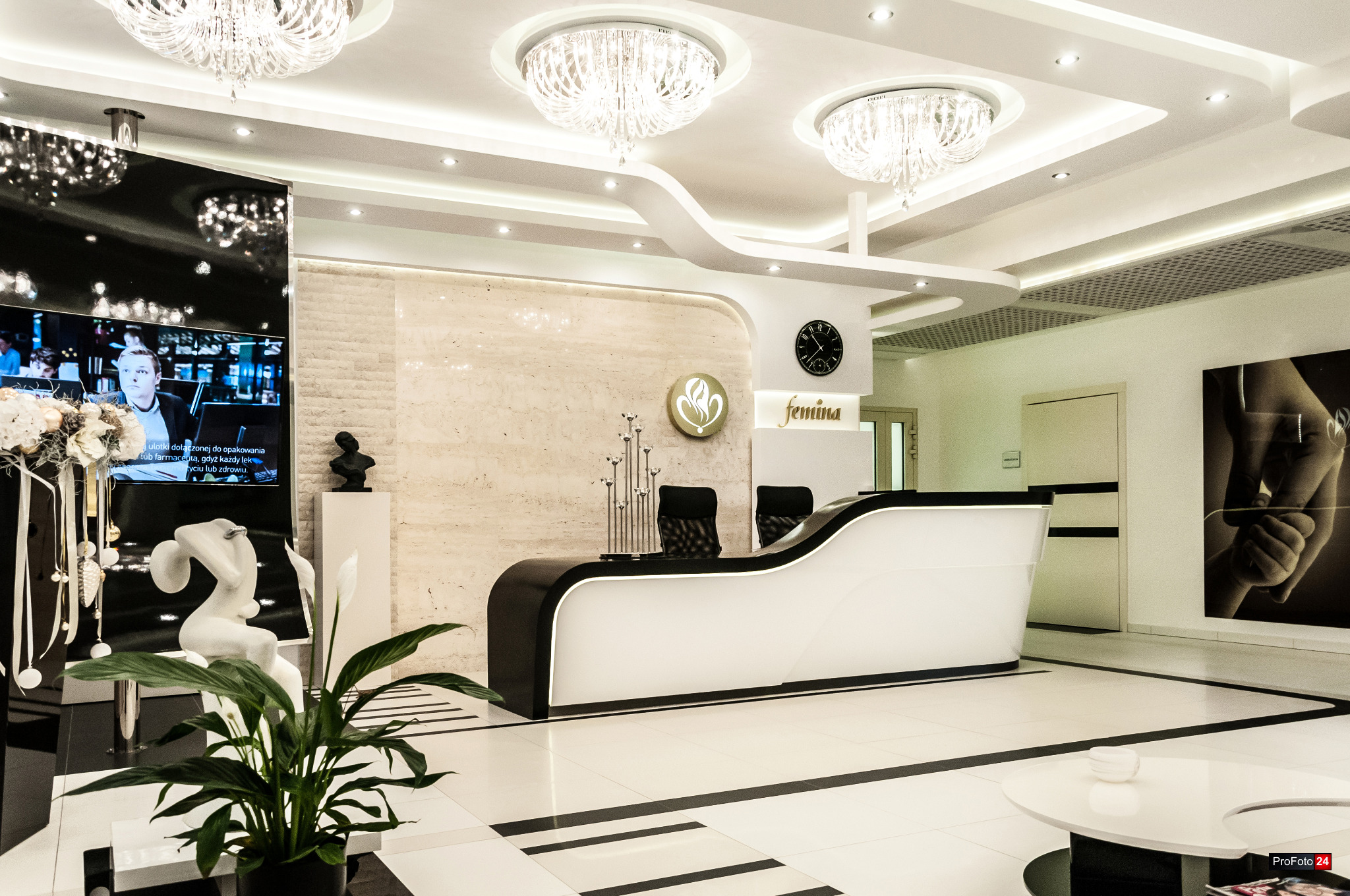 Eleganckie wnętrze recepcji w Krakowie, z biało-czarną ladą recepcyjną o falistym kształcie, oświetloną kryształowymi żyrandolami, z marmurową ścianą w tle i dekoracyjnymi elementami jak rzeźba...