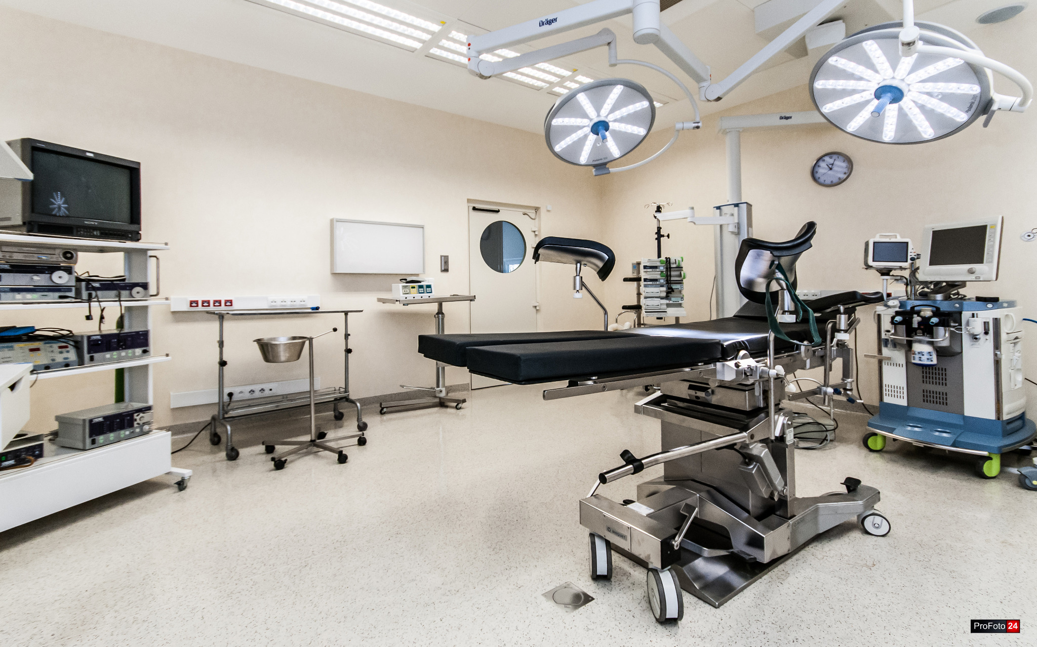 Wnętrze sali operacyjnej z nowoczesnym stołem operacyjnym, lampami zabiegowymi Dräger, aparaturą medyczną i monitorem, przygotowane do zabiegu.