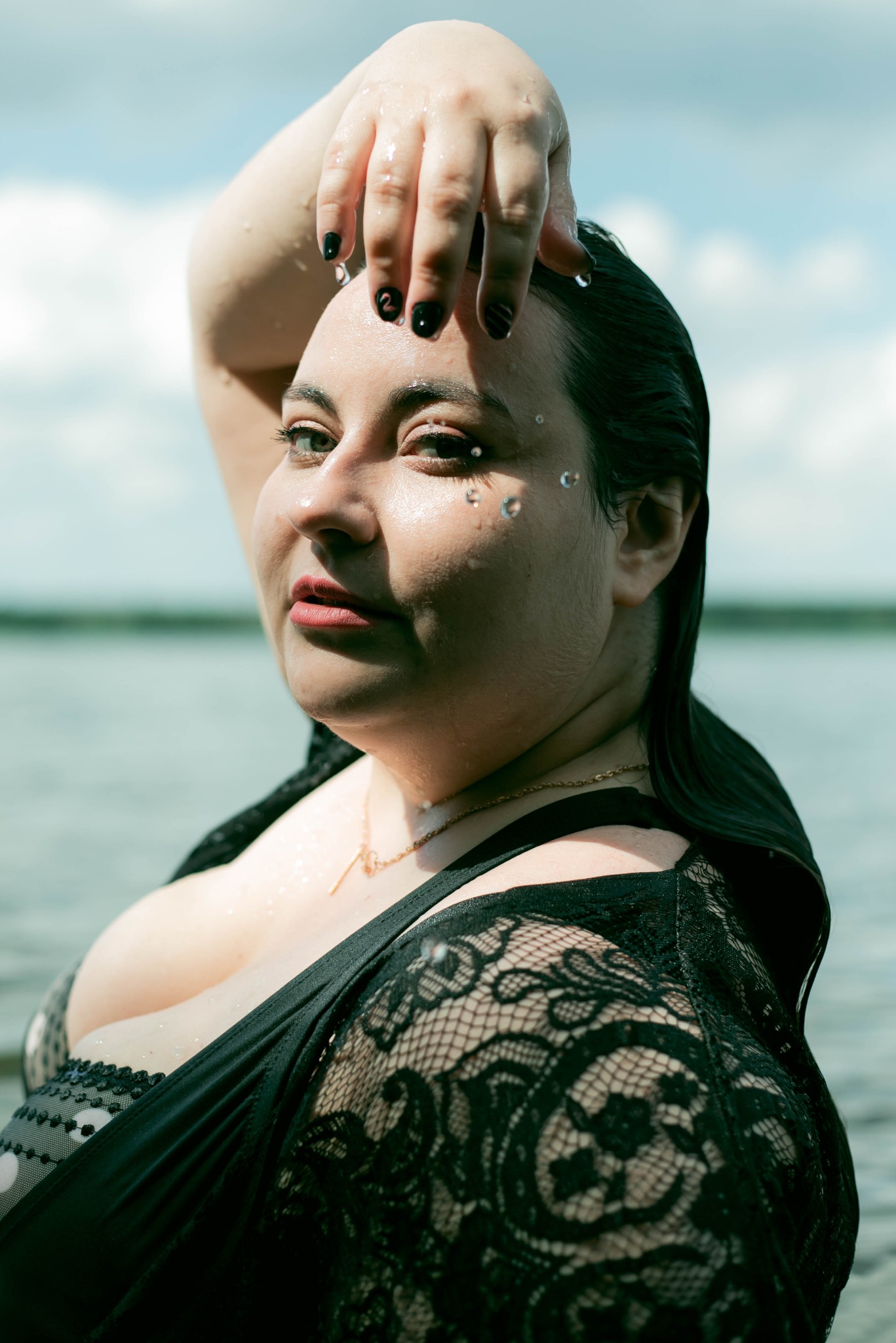 Portret kobiety w wodzie, czarna koronkowa narzutka, woda skapuje z twarzy, ozdobne kryształki na policzkach, manicure w czarnym kolorze.