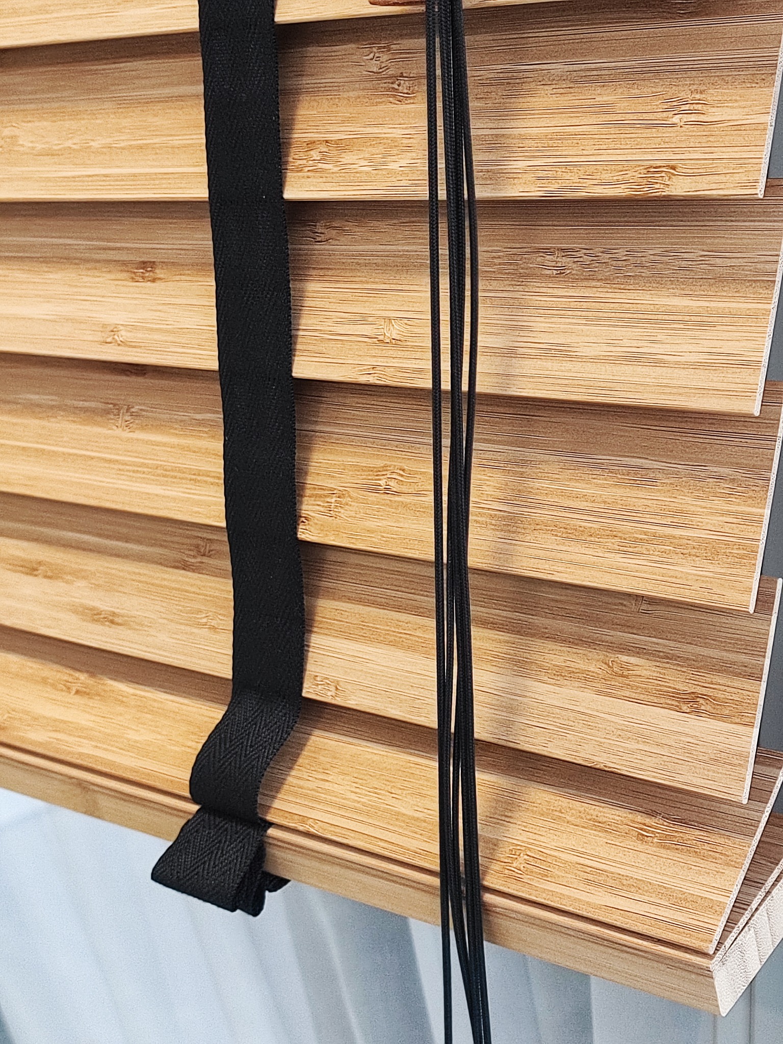 Bambusowe żaluzje drewniane z czarnymi sznurkami i taśmą, zamontowane w Woli Baranowskiej, widoczne z bliska.