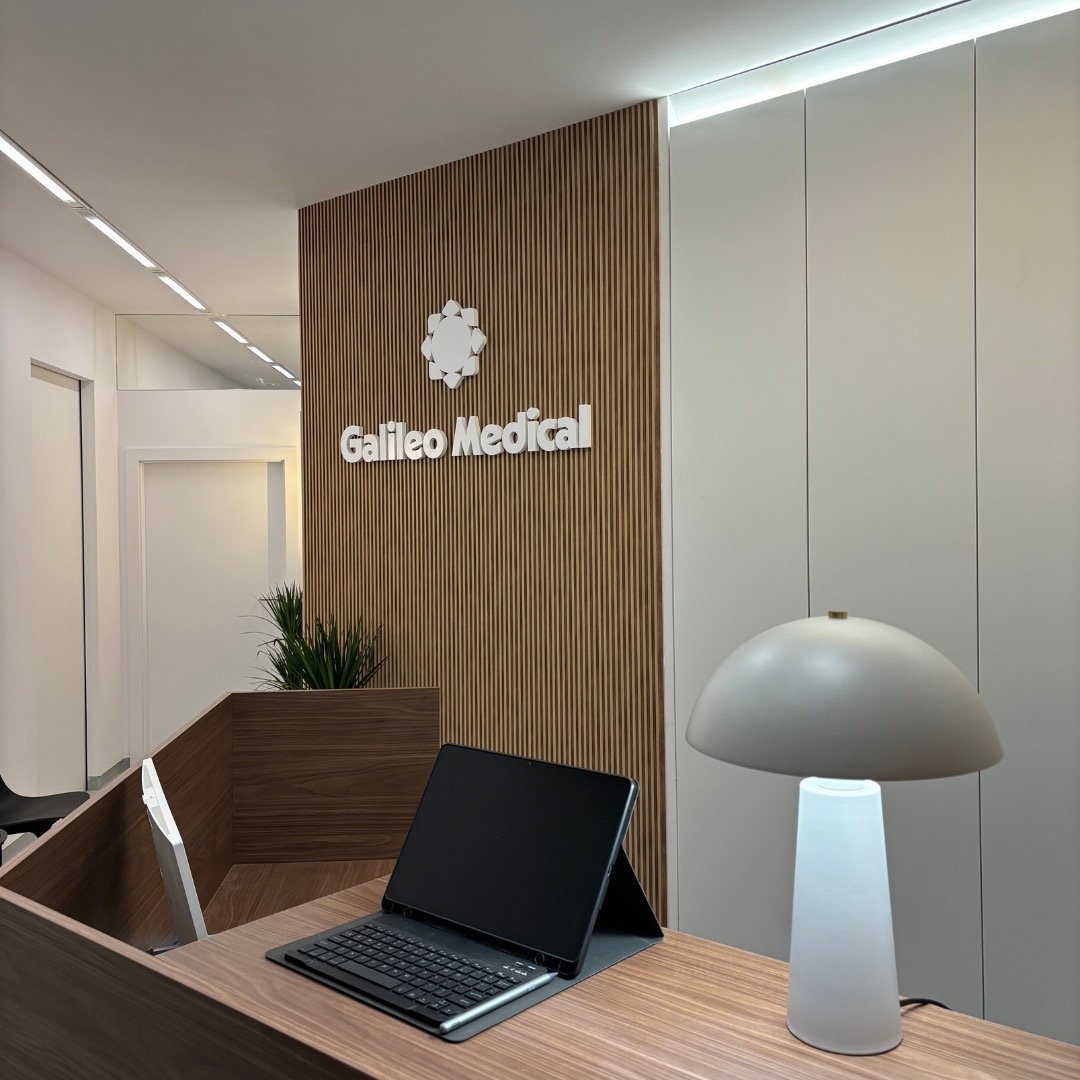 Recepcja kliniki medycznej z logo Galileo Medical na drewnianej ścianie, biurko z tabletem i lampką w stylu retro.