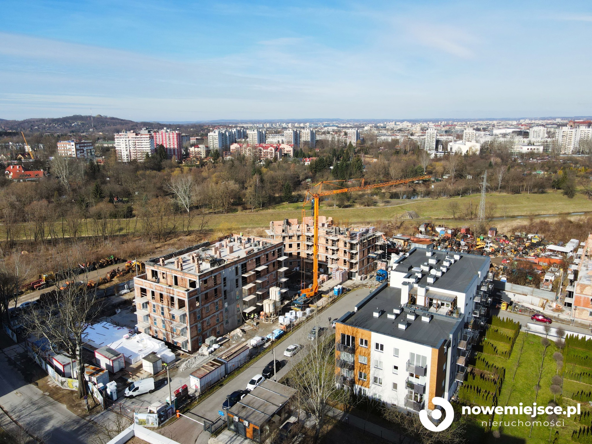 Panorama budowy osiedla mieszkaniowego z pomarańczowym dźwigiem na tle miejskiego krajobrazu w słoneczny dzień.