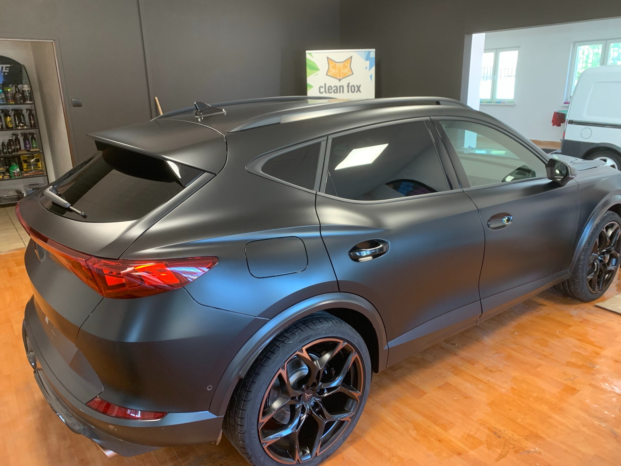 Ciemnoszary samochód typu SUV z matowym wykończeniem, widok z tyłu i boku, z widocznymi czarnymi felgami i logo 'clean fox' w tle.