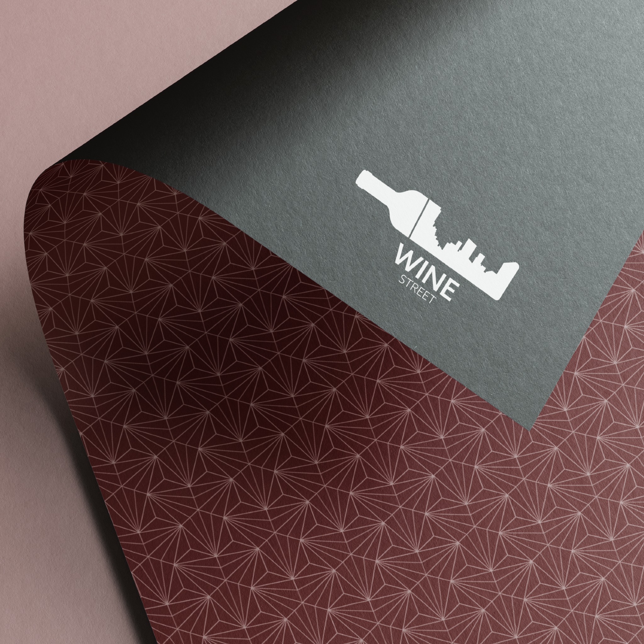 Elegancka wizytówka z logo Wine Street przedstawiającym butelkę wina na tle panoramy miasta, na bordowym tle z geometrycznym wzorem.