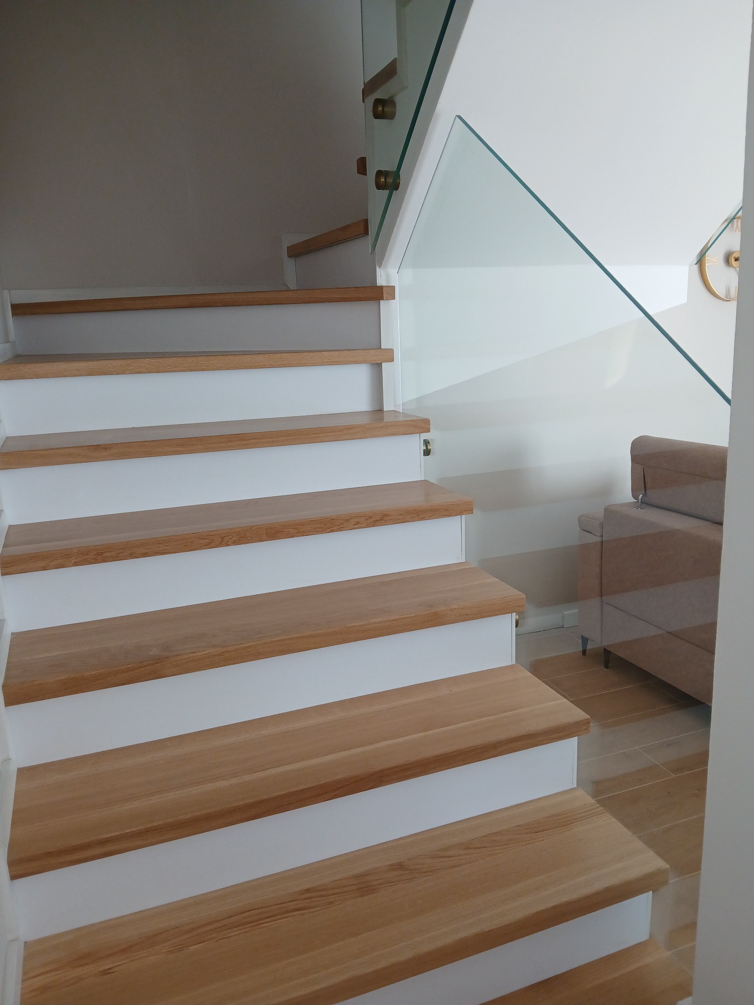 Nowoczesne schody z drewnianymi stopniami i szklaną balustradą, widok z dołu, jasne wnętrze z elementami dekoracyjnymi w tle.