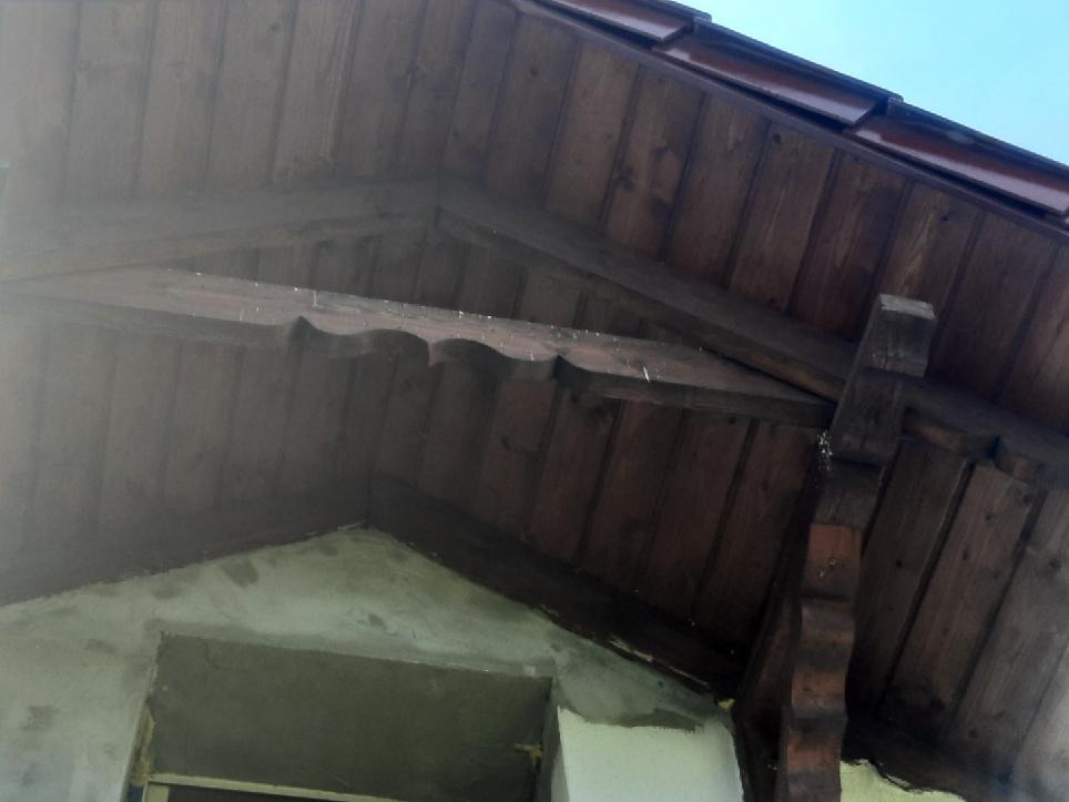 Fragment drewnianej konstrukcji dachu z widoczną więźbą i deskowaniem, z elementami obróbki dekoracyjnej, w trakcie budowy lub remontu budynku.