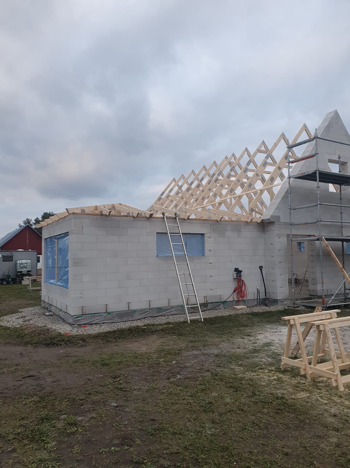 Wznoszenie ścian z bloczków betonu komórkowego, widoczna konstrukcja dachu, rusztowanie i drabina oparta o ścianę budynku w trakcie budowy.