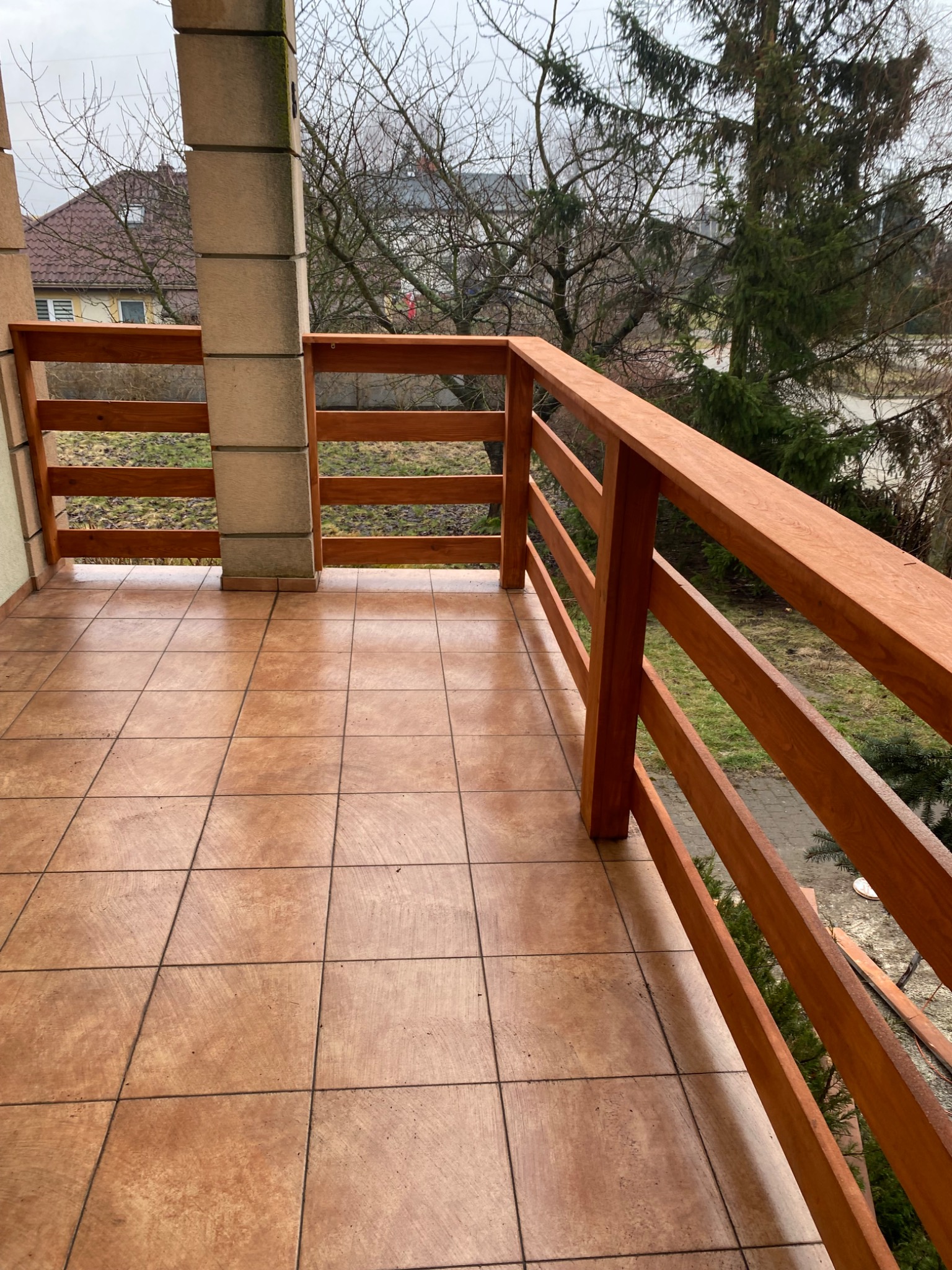 Wykończony balkon z terakotą i drewnianą balustradą w Starogardzie Gdańskim, widok na ogród w pochmurny dzień.