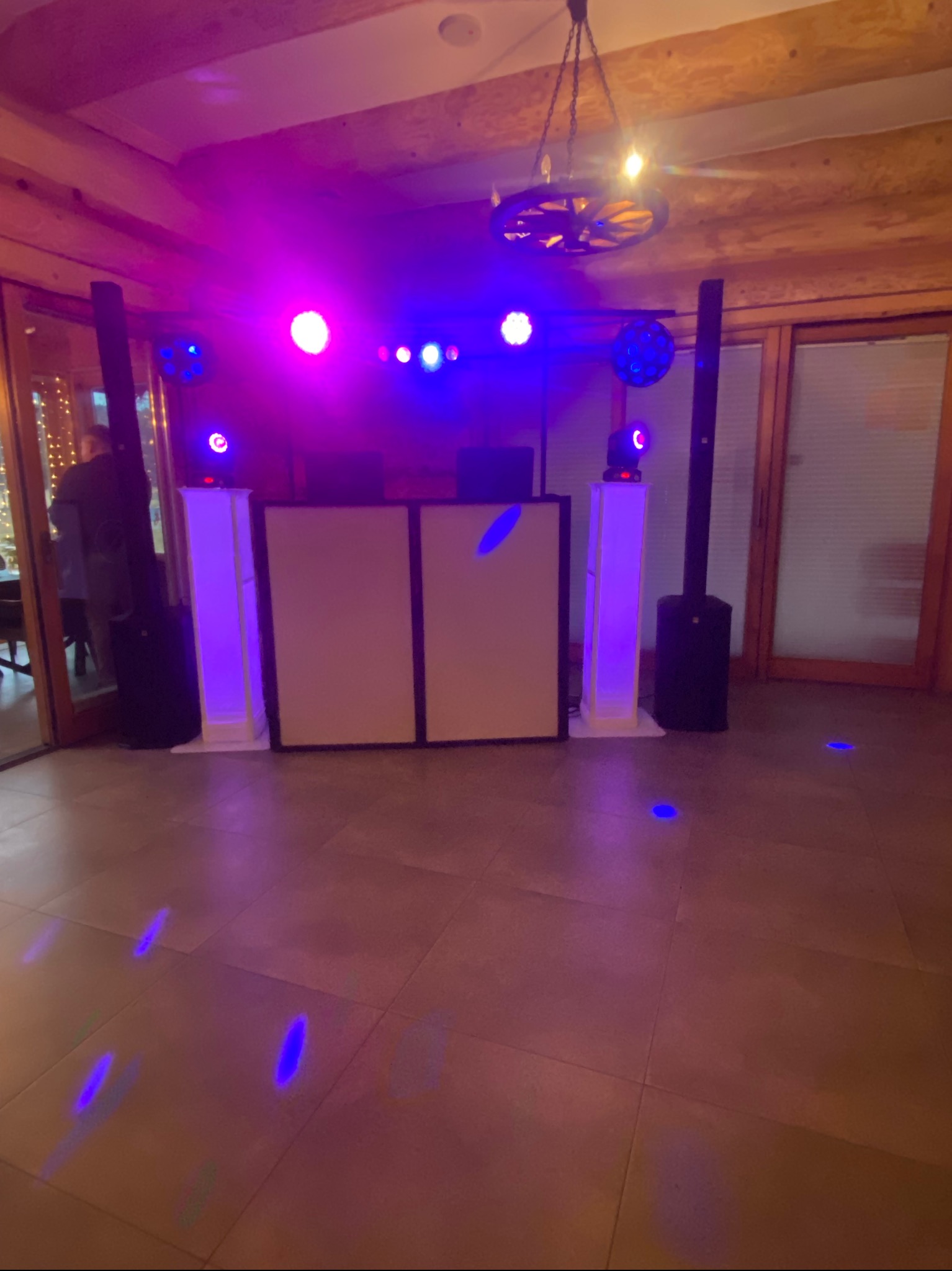 Sala z parkietem i sceną oświetloną na fioletowo. Widoczne głośniki, konsoleta DJ-a i dekoracyjna lampa z koła od wozu. Przygotowania do imprezy.