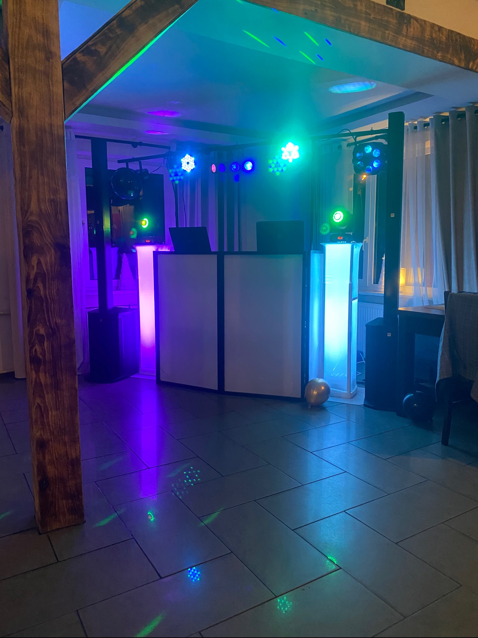 Rozstawiony sprzęt nagłośnieniowy i oświetleniowy w pomieszczeniu z drewnianą konstrukcją. Widoczne kolumny, konsoleta DJ-ska i efekty świetlne.