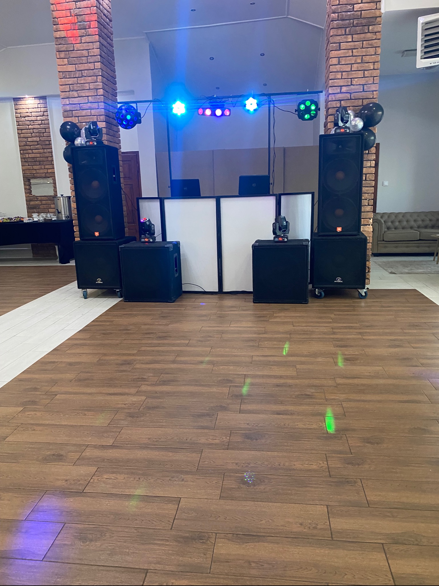 Sala bankietowa z nagłośnieniem: kolumny, subwoofery, oświetlenie sceniczne i dekoracyjne. Parkiet z brązowych paneli, ceglane kolumny, dekoracja balonowa.