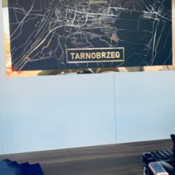 Mapa Tarnobrzega w złotej ramie na ścianie biura nieruchomości, na biurku ulotki i pieczątki.