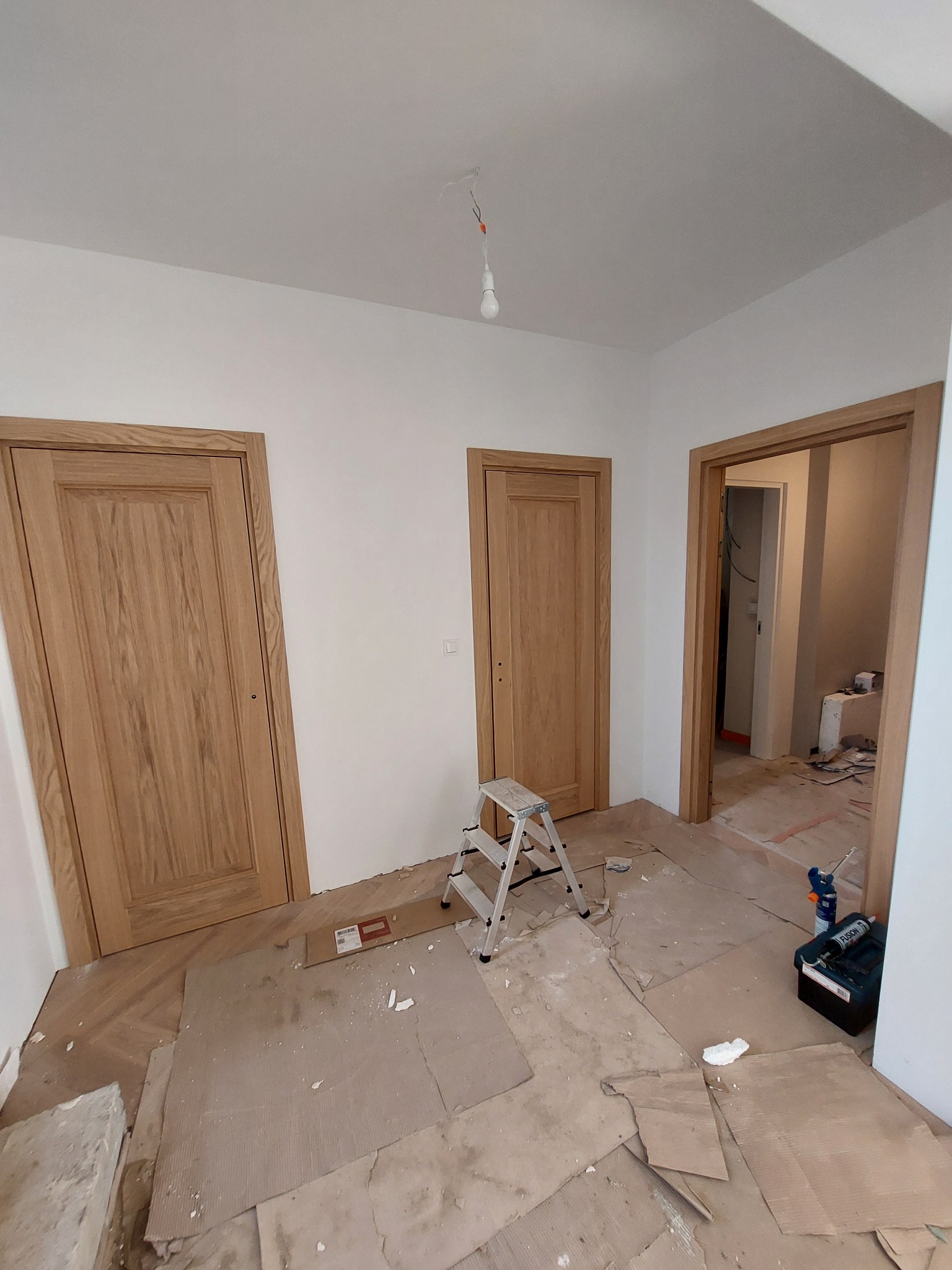 Montaż trzech drewnianych drzwi wewnętrznych w nowym domu. Na podłodze resztki po montażu i drabina. Widok na dwa pomieszczenia.