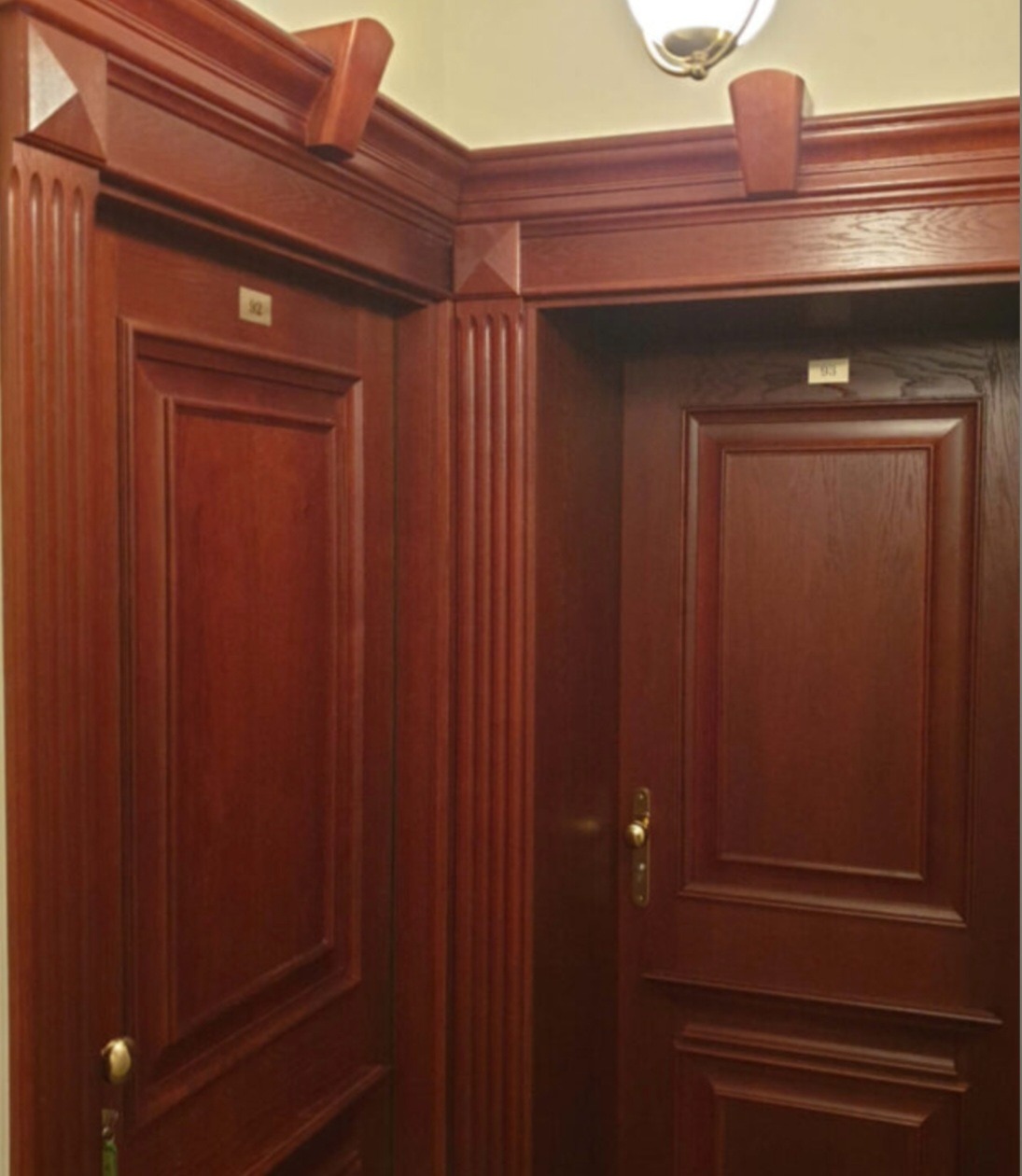 Eleganckie, mahoniowe drzwi wewnętrzne z numerami pokoi w Gdańsku. Klasyczny design z frezowanymi panelami i dekoracyjnymi listwami.