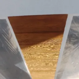 Drewnopodobny sufit z widocznym zabezpieczeniem folią malarską, fragment białego sufitu i cegieł na podłodze.