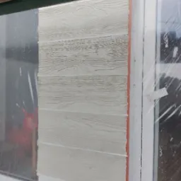 Fragment ściany z panelami imitującymi drewno, montowanymi przy oknie, widoczne uszczelnienie pomarańczową pianką montażową.