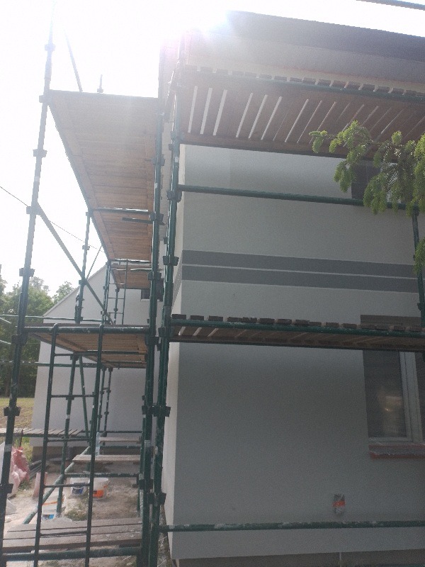 Dom w trakcie prac remontowych, widoczne rusztowania, pomalowana elewacja na szaro, ślady farby na rusztowaniach.