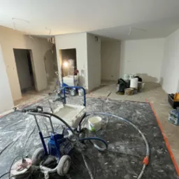 Wnętrze w trakcie szpachlowania maszynowego, widoczne agregaty szpachlarskie, zakryta folią podłoga, ściany przygotowane do malowania.