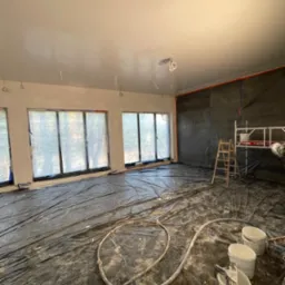 Przygotowanie do malowania biura: rozłożona folia ochronna, wiadra z farbą, szpachelki, zaklejone okna folią, drabina i rusztowanie w tle.