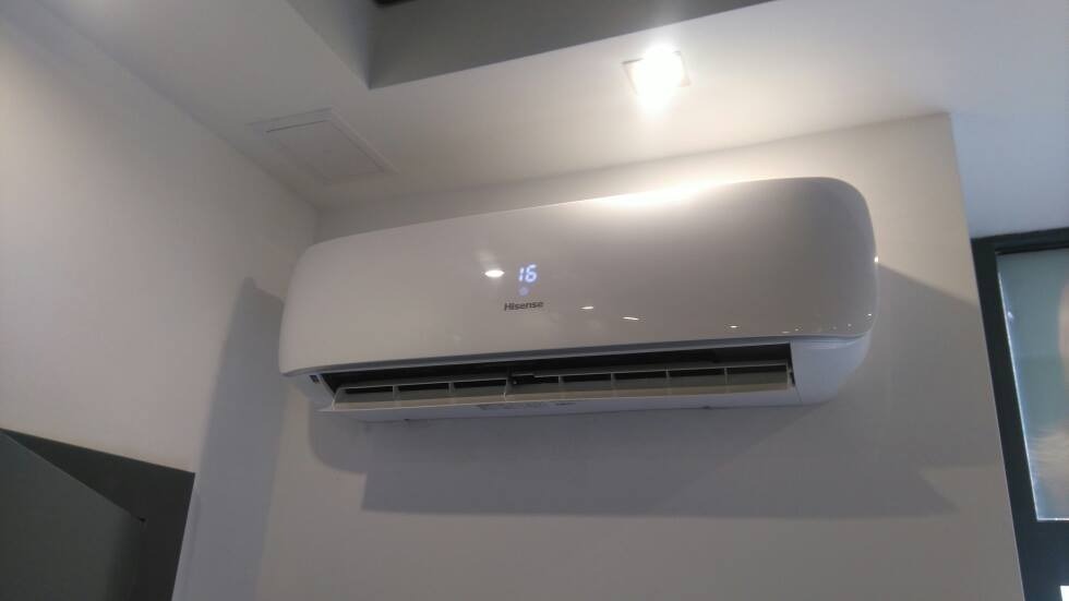 Biały klimatyzator Hisense z wyświetlaczem temperatury 16 stopni Celsjusza zamontowany na białej ścianie w nowoczesnym wnętrzu.