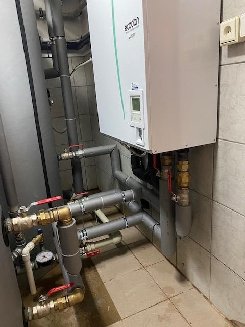 Nowoczesny piec grzewczy EcoDan A+++ z licznymi rurami i zaworami w kotłowni wyłożonej jasnymi płytkami.