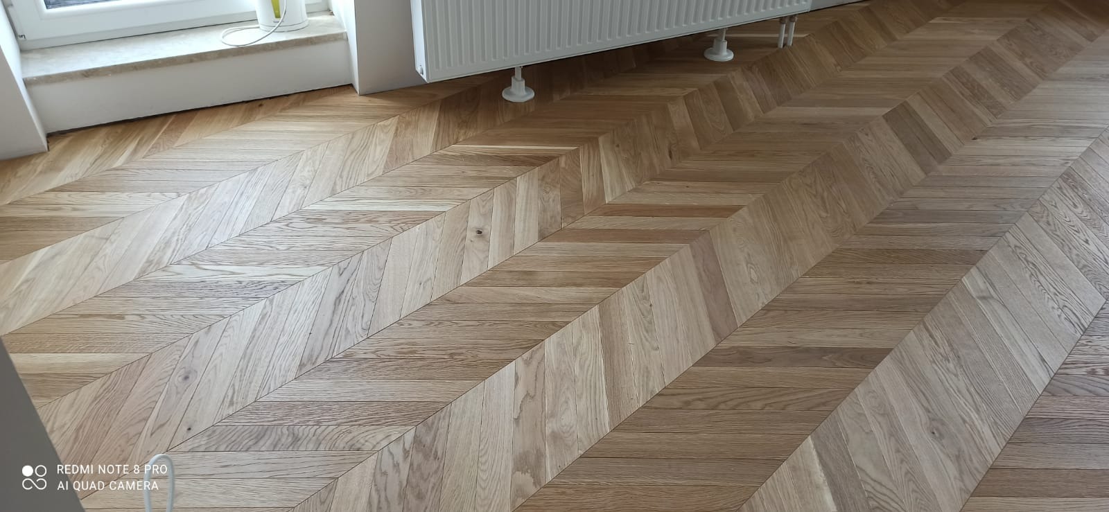 Ułożony parkiet w jodełkę francuską, widoczny fragment okna i grzejnika.