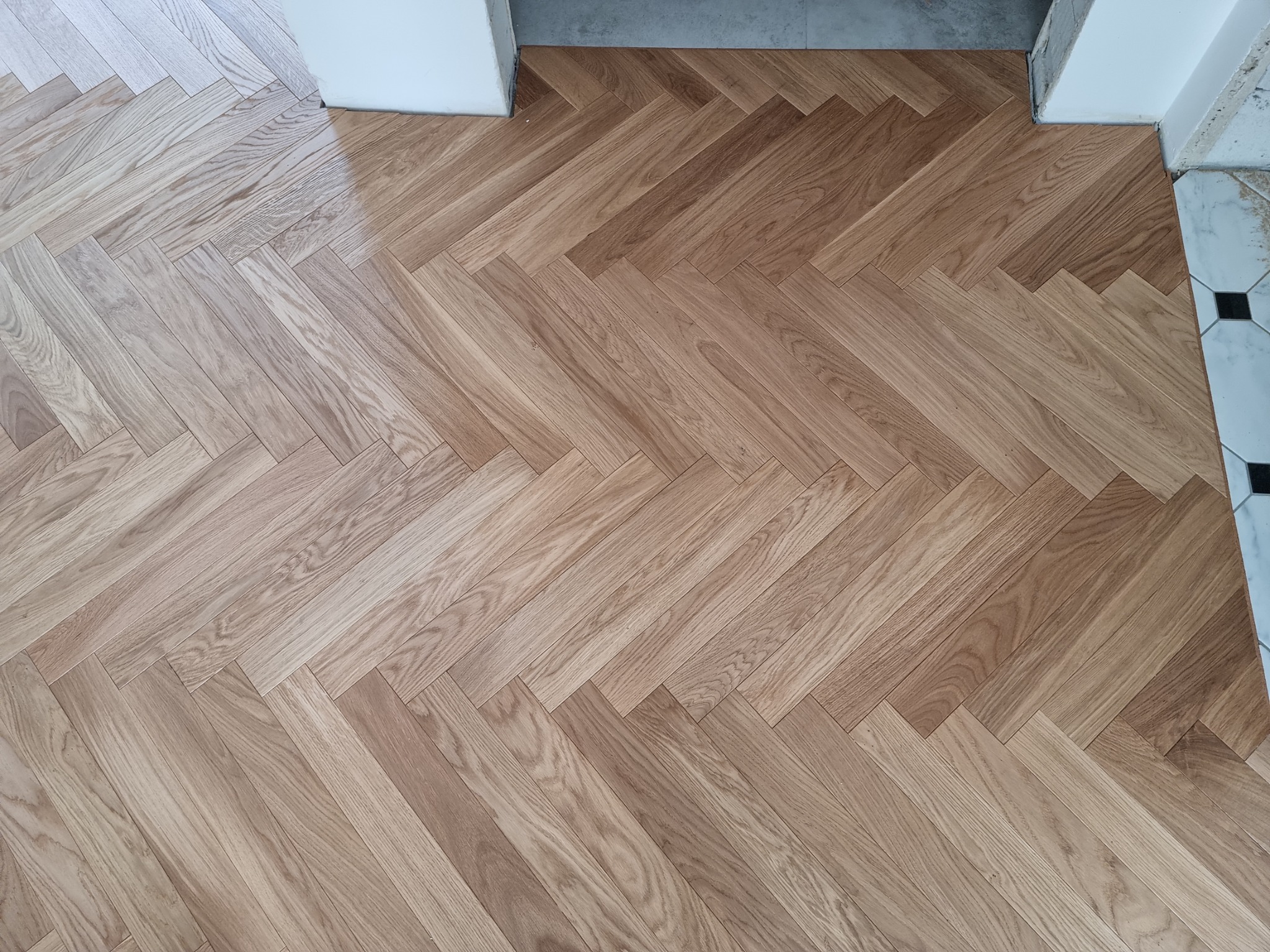 Ułożony parkiet w jodełkę francuską, widoczne łączenie z innym rodzajem podłogi przy progu.