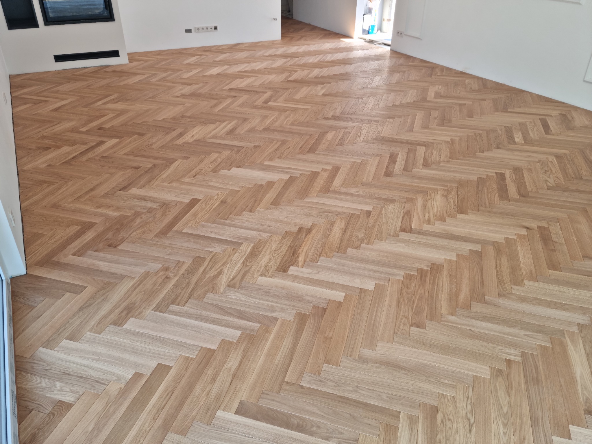 Ułożony parkiet w jodełkę francuską, jasne drewno, widok na przestronne, jasne wnętrze z białymi ścianami i otwartymi drzwiami.