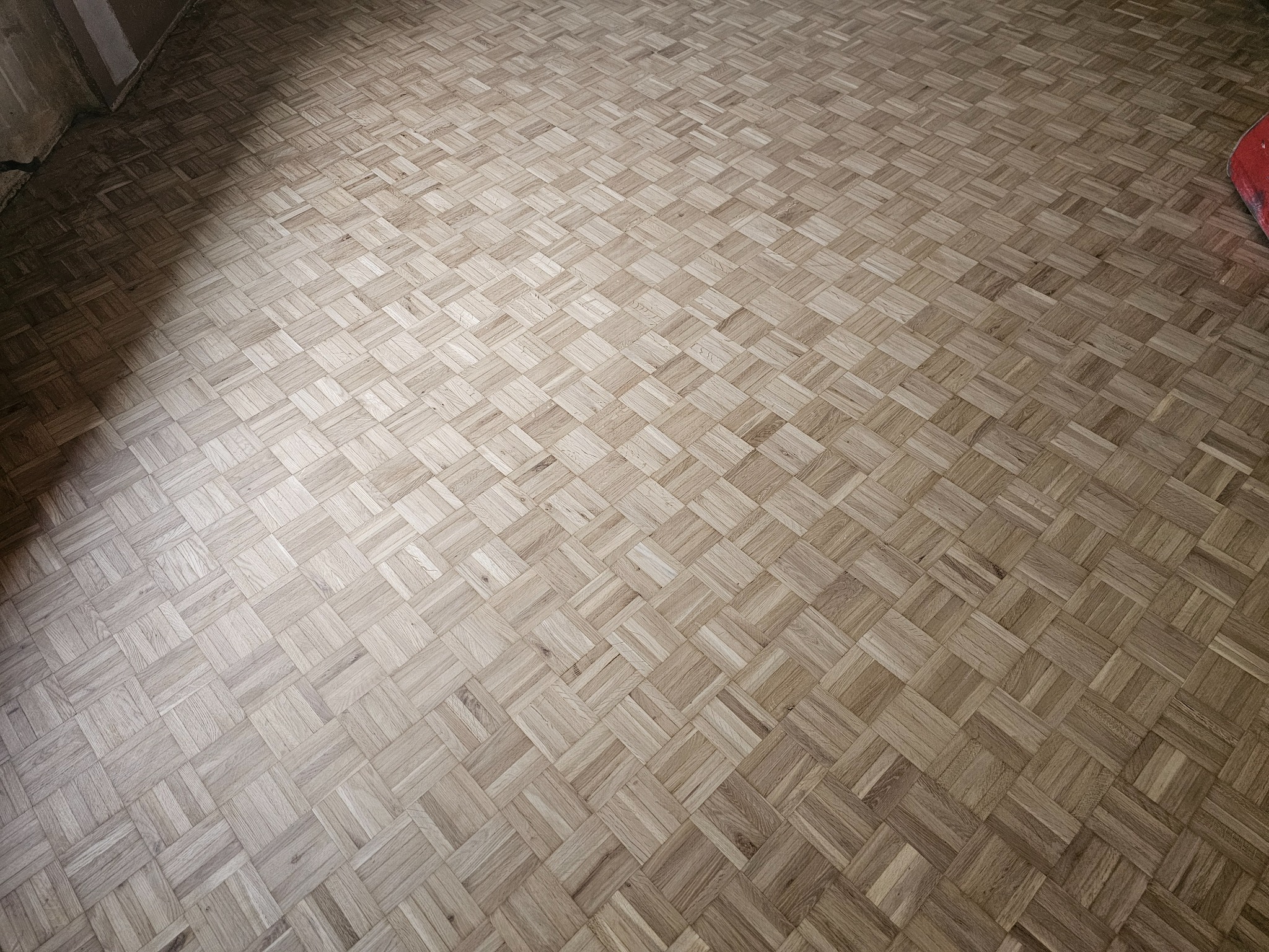 Parkiet ułożony w jodełkę francuską z jasnego drewna, widok z góry, z delikatnym cieniem w lewym górnym rogu.