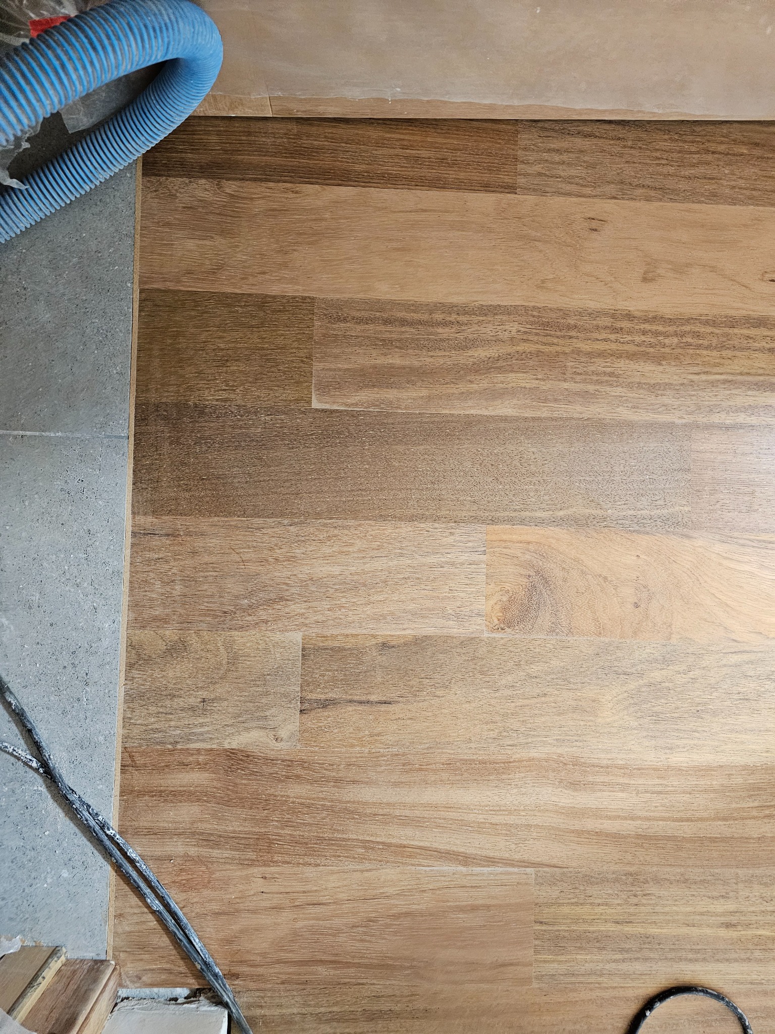 Fragment podłogi z drewnianych desek w trakcie renowacji, widoczny wąż od odkurzacza przemysłowego i przewody, szlifowana powierzchnia z widocznymi słojami.