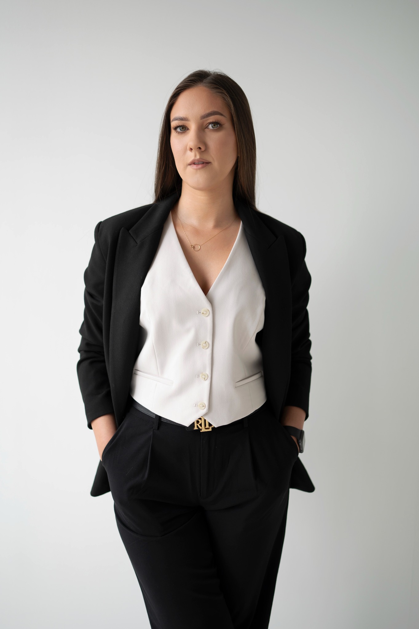 Portret kobiety w czarnym garniturze, białej kamizelce i złotym pasku z logo na jasnym tle. Profesjonalny wizerunek, idealny dla doradcy finansowego.