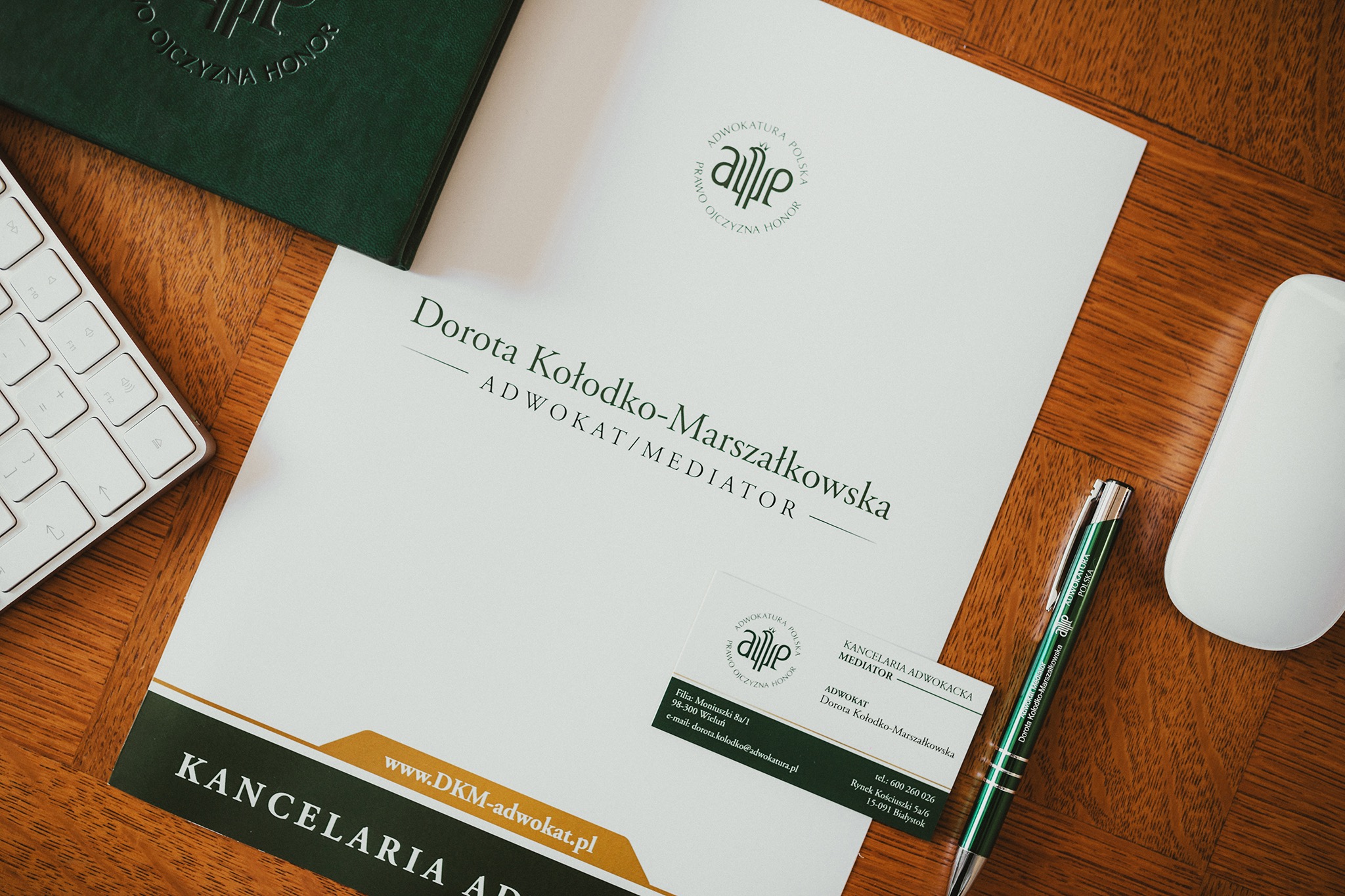 Biurko z dokumentami kancelarii adwokackiej Doroty Kołodko-Marszałkowskiej, wizytówką, długopisem, klawiaturą i myszką komputerową.