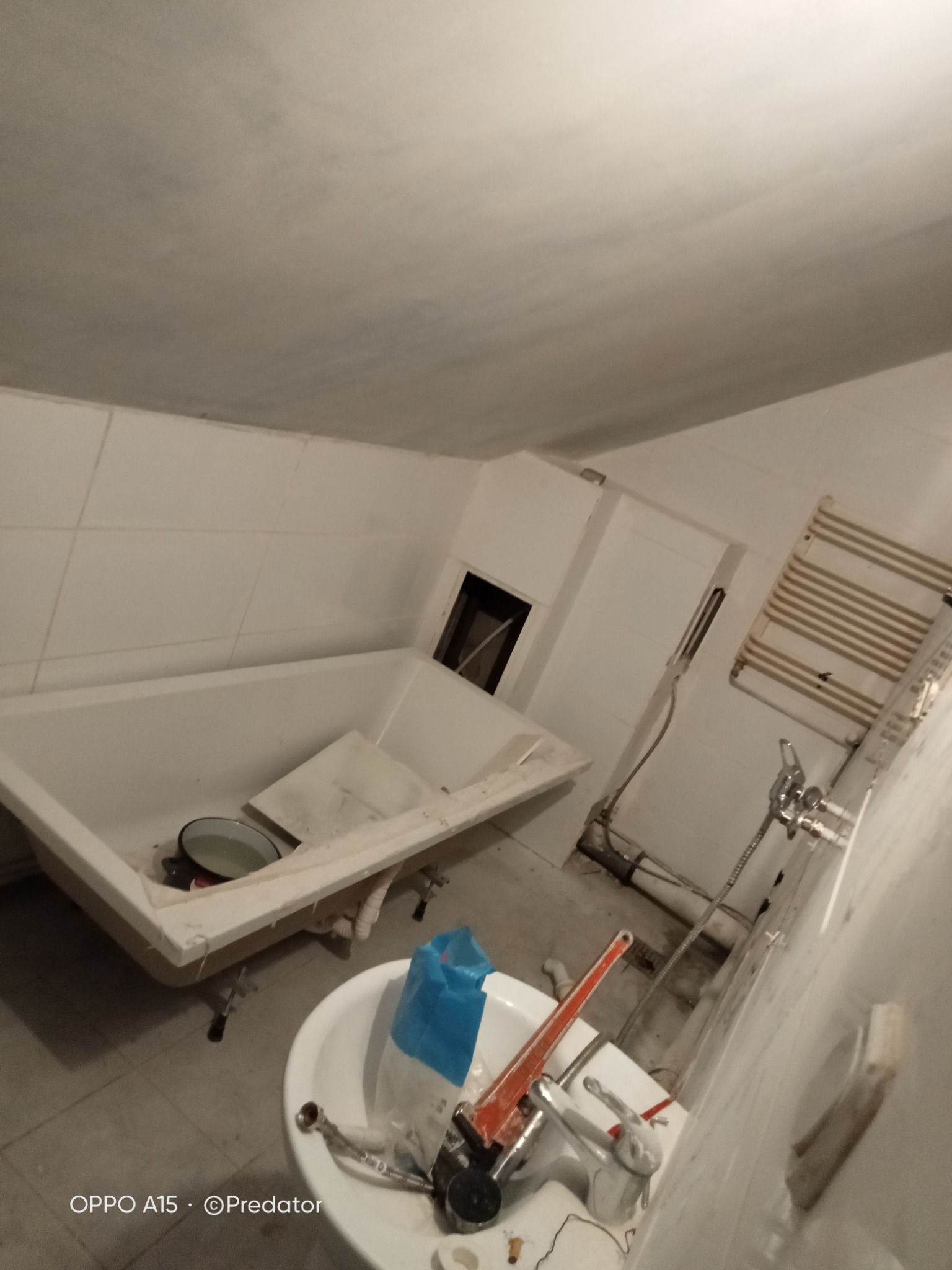 Łazienka w trakcie remontu: widoczna wanna z resztkami gruzu, niedokończona umywalka z narzędziami i nieestetyczne oświetlenie.