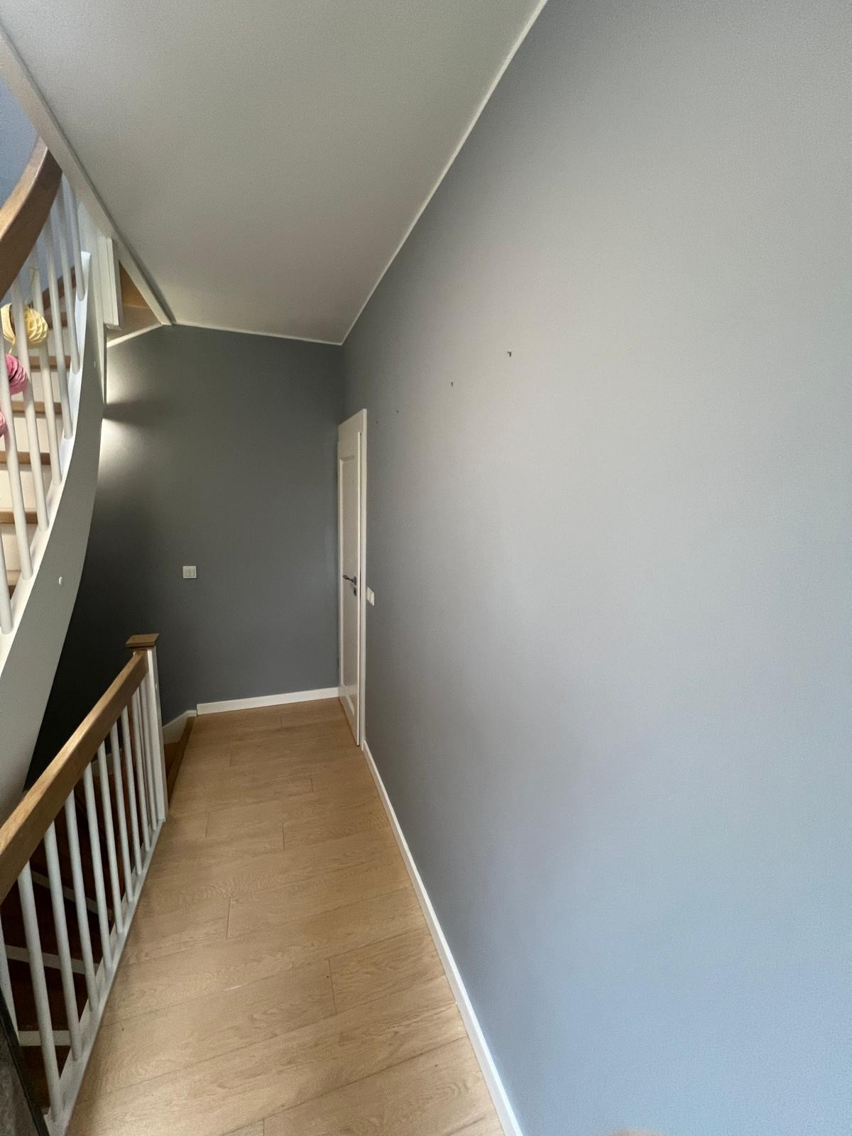 Klatka schodowa po świeżym malowaniu ścian na szaro i niebiesko, z widocznymi schodami z drewnianą barierką i panelami podłogowymi w odcieniach beżu.