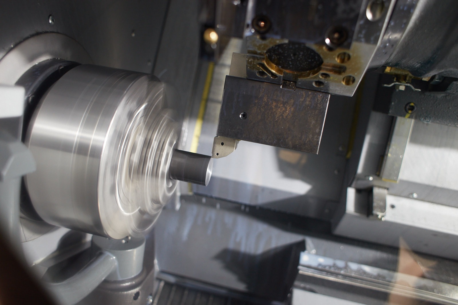 Metalowy element obrabiany na tokarce CNC, widoczne wióry i chłodziwo, precyzyjna obróbka skrawaniem.