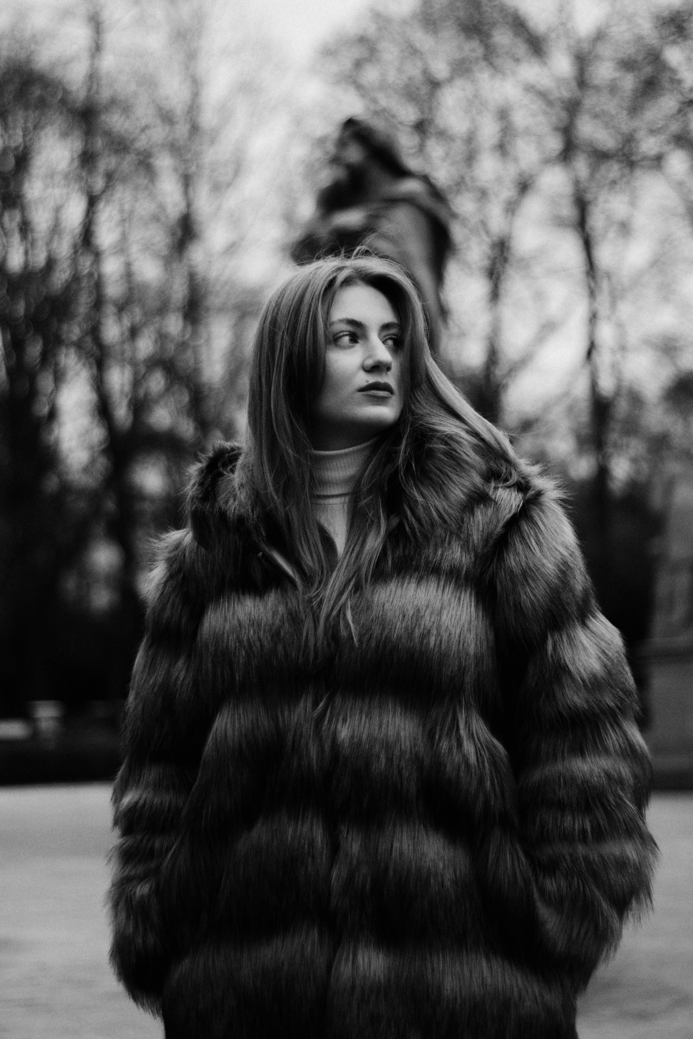 Czarno-białe zdjęcie kobiety w futrze, zamyślona poza, park w tle