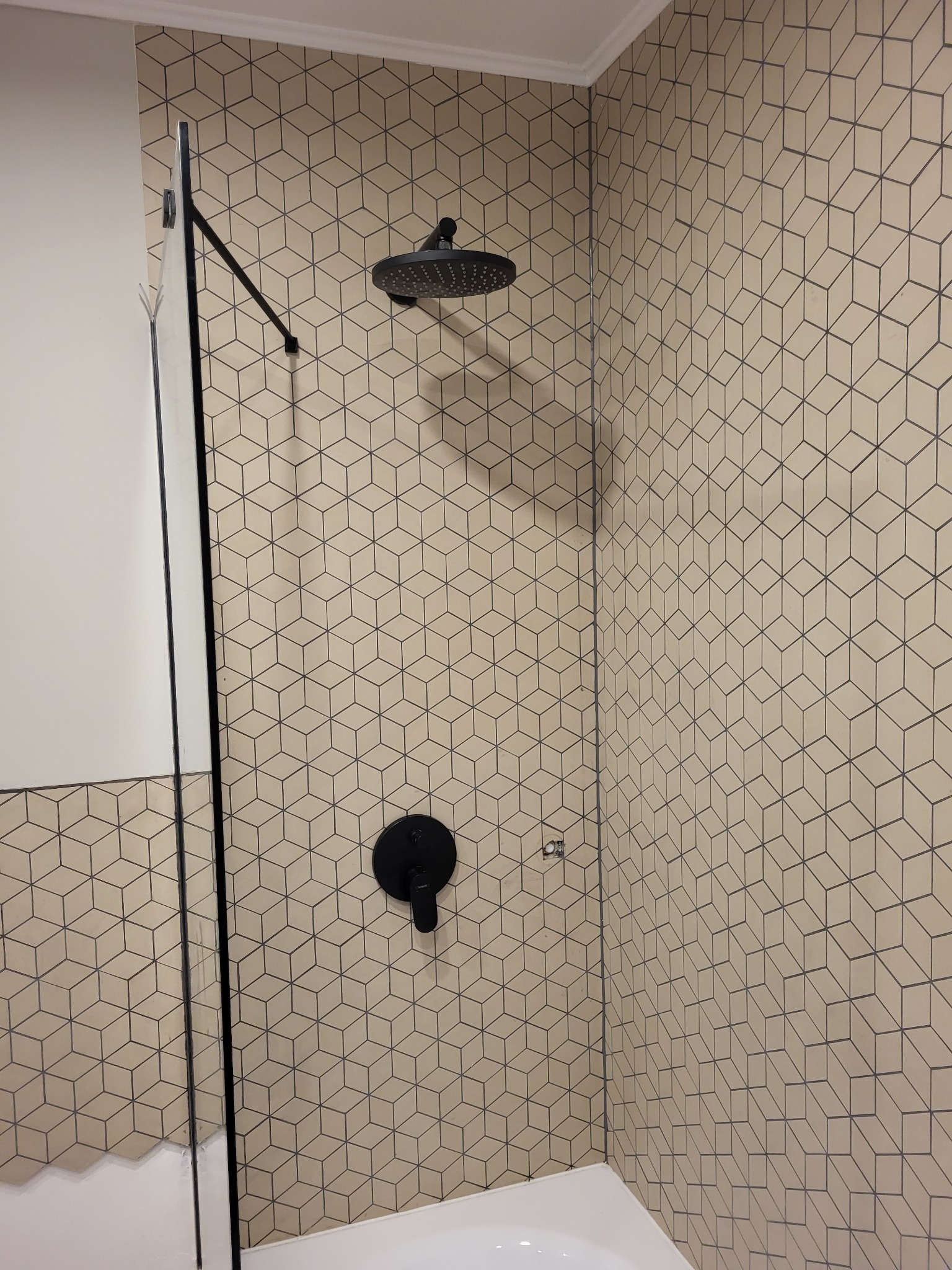 Kabina prysznicowa walk-in z czarną armaturą i geometrycznymi płytkami w odcieniach beżu i szarości.