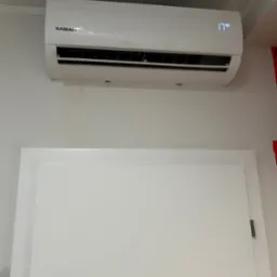 Biały klimatyzator marki Kaisai zamontowany na ścianie nad białymi drzwiami, wyświetlający temperaturę 17 stopni Celsjusza.