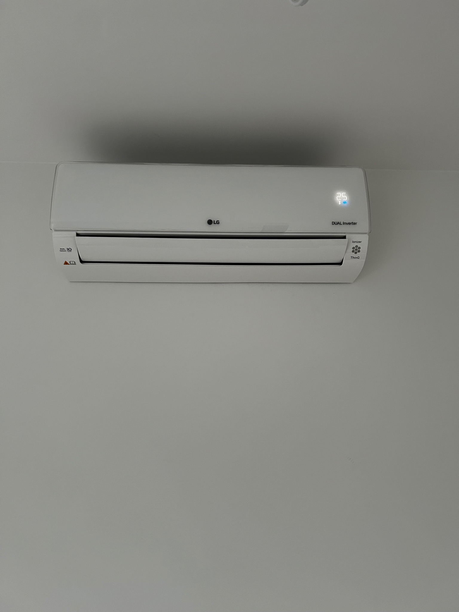 Biała jednostka wewnętrzna klimatyzacji LG Dual Inverter zamontowana na jasnej ścianie, wyświetlająca temperaturę 25 stopni Celsjusza.