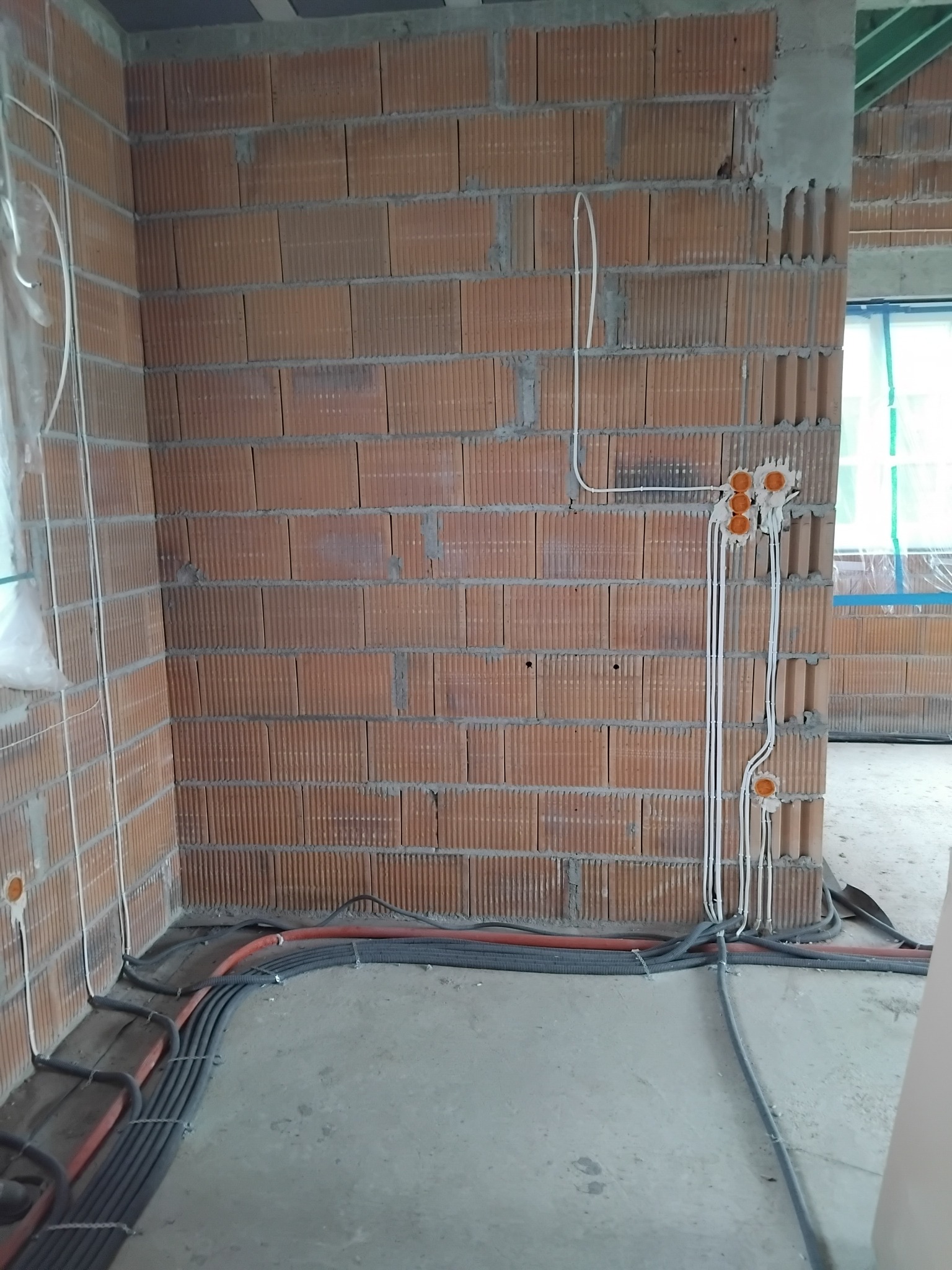 Wewnętrzne ściany z pustaków ceramicznych z widocznymi puszkami elektrycznymi i przewodami w peszlach, ułożonymi wzdłuż podłogi w surowym stanie.