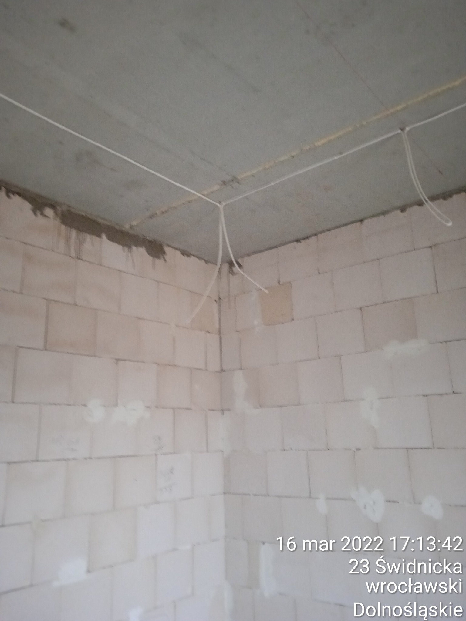 Wnętrze w stanie surowym we Wrocławiu, widoczne kable elektryczne wystające z sufitu i ściany z bloków, przygotowane do dalszych prac wykończeniowych.